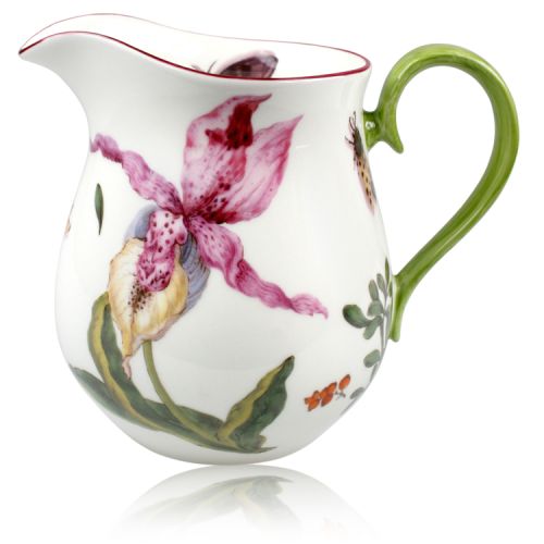 Milk jug on table cloth with bowl of lemons and flowers in background. 